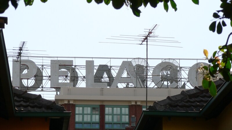 The white letters of the sign on the roof an old factory, seen between tress and houses