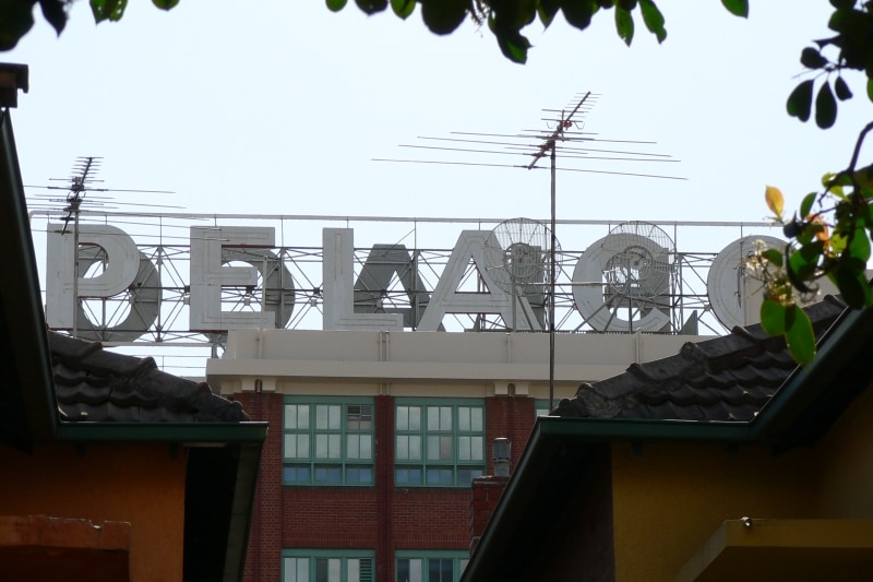 The white letters of the sign on the roof an old factory, seen between tress and houses