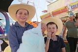 Two young boys wearing shirts and cowboy hats tuck into a stick of blue fairy floss.
