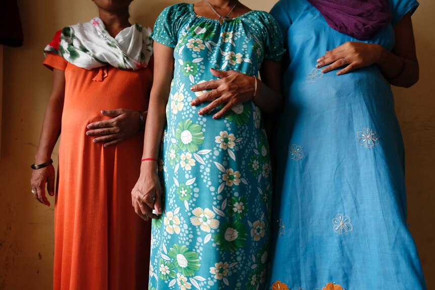 Three pregnant women wearing colourful dresses standing side-by-side