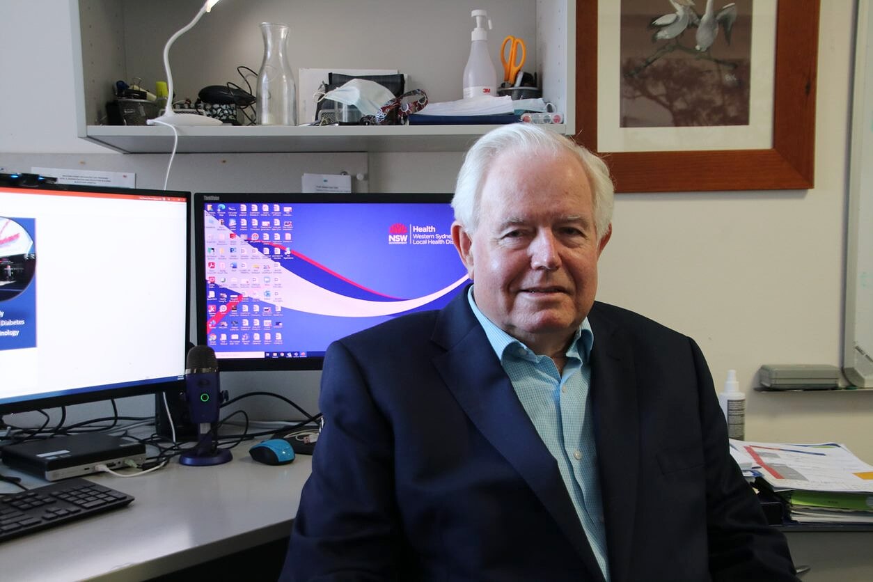 an elderly man sitting down at his desk and looking at the camera