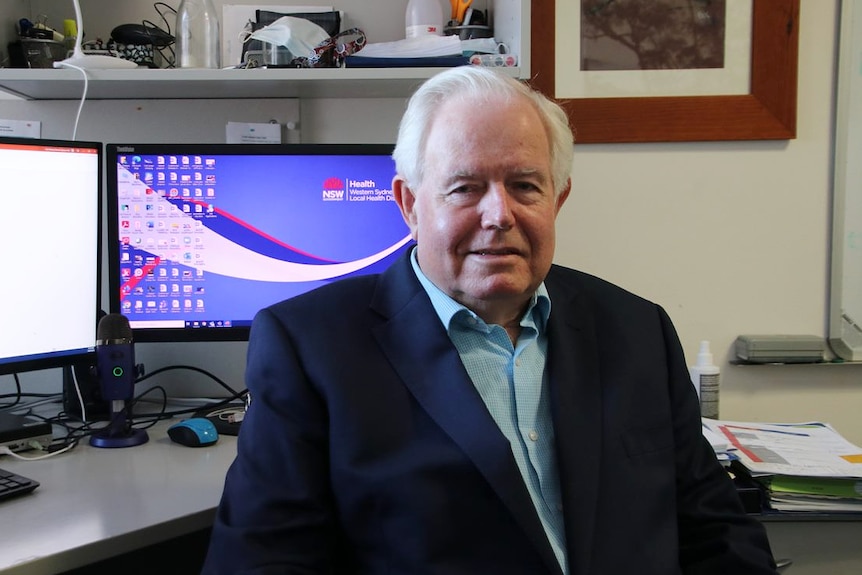 an elderly man sitting down at his desk and looking at the camera