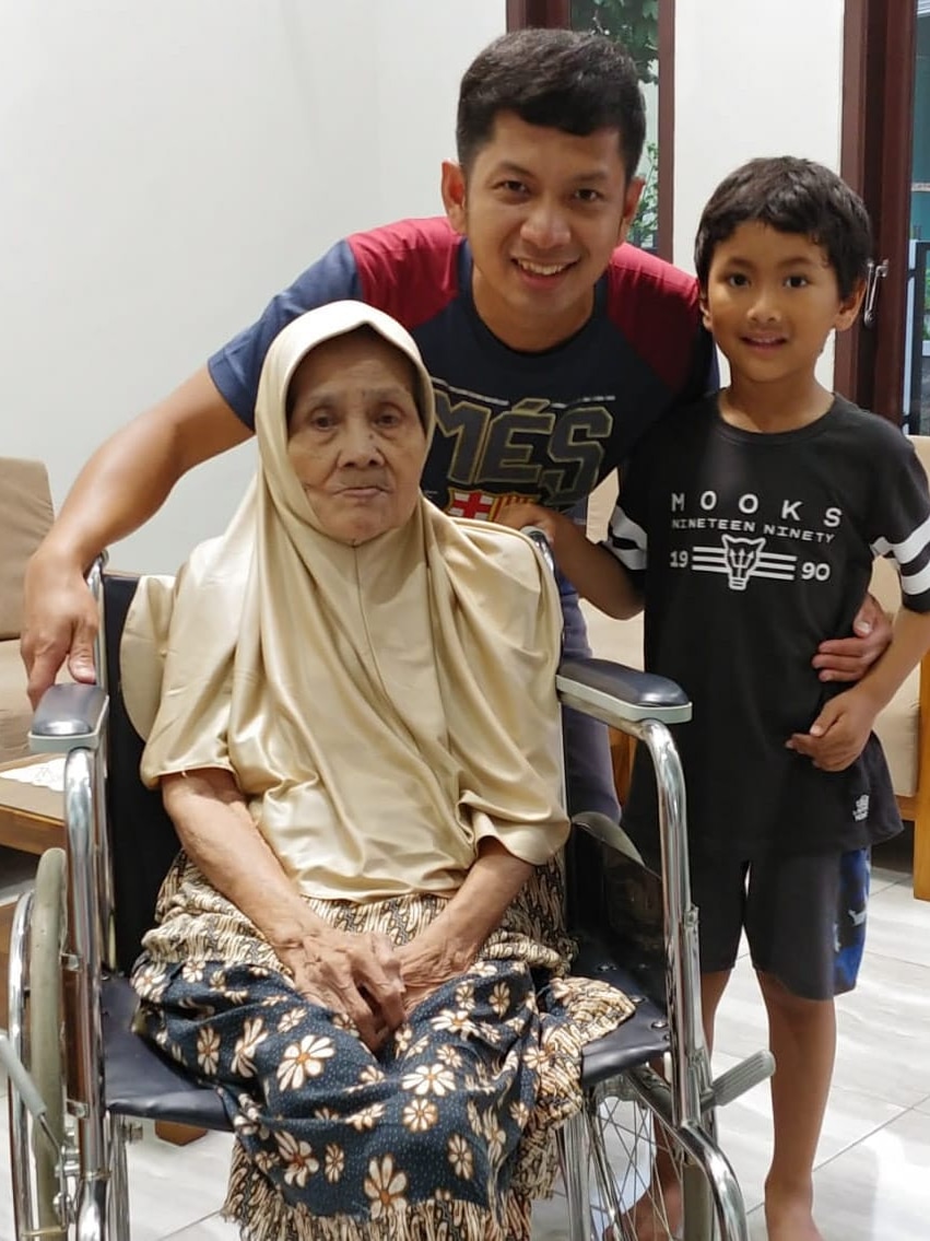  Didi's grandmother sitting in a wheelchair with Didi and his son standing behind her.