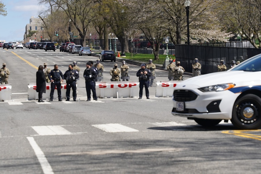 Police and army line the street behind a police car.