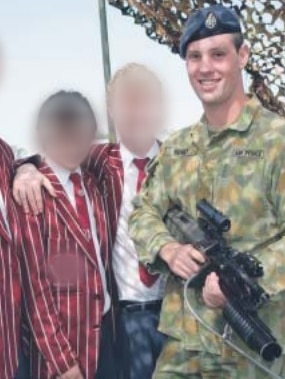 Jared with camouflage uniform and weapon standing beside three boys.