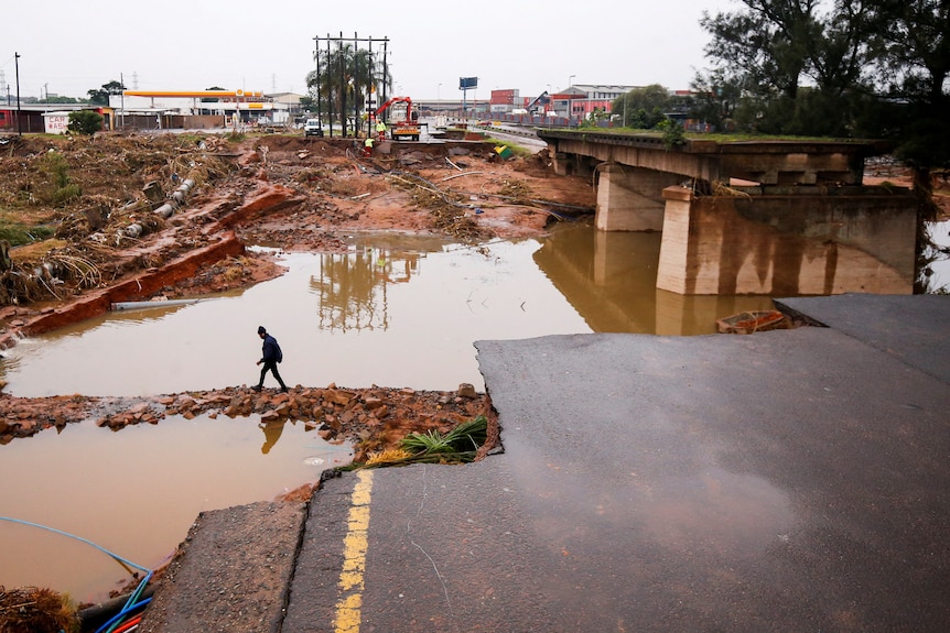 Un uomo cammina intorno a un ponte danneggiato da un'alluvione