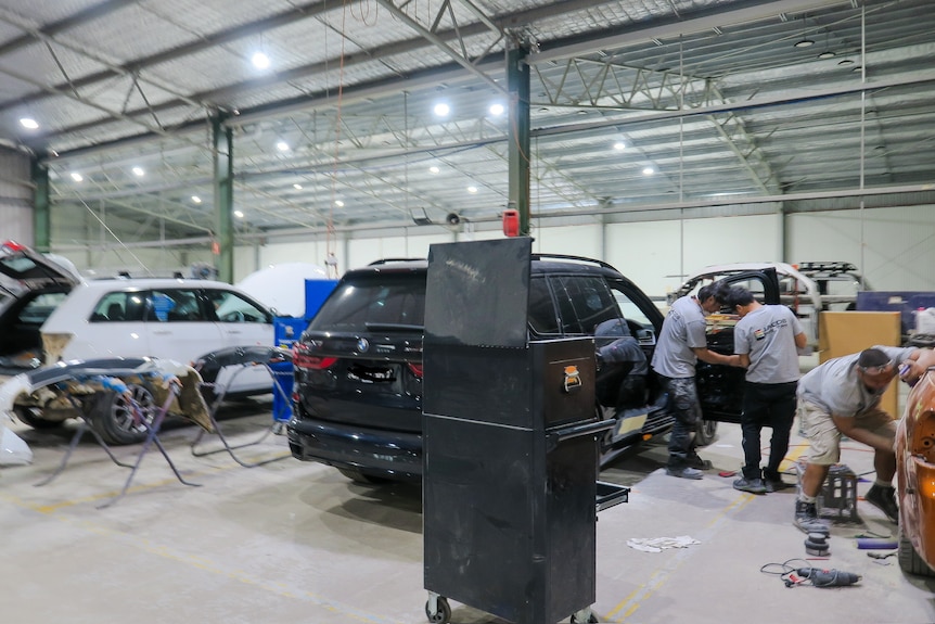Workers sand back a black four-wheel-drive car in a panel beaters workshop