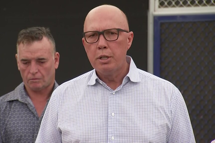 Peter Dutton wearing a white collared shirt with black glasses mid-sentence at a press conference