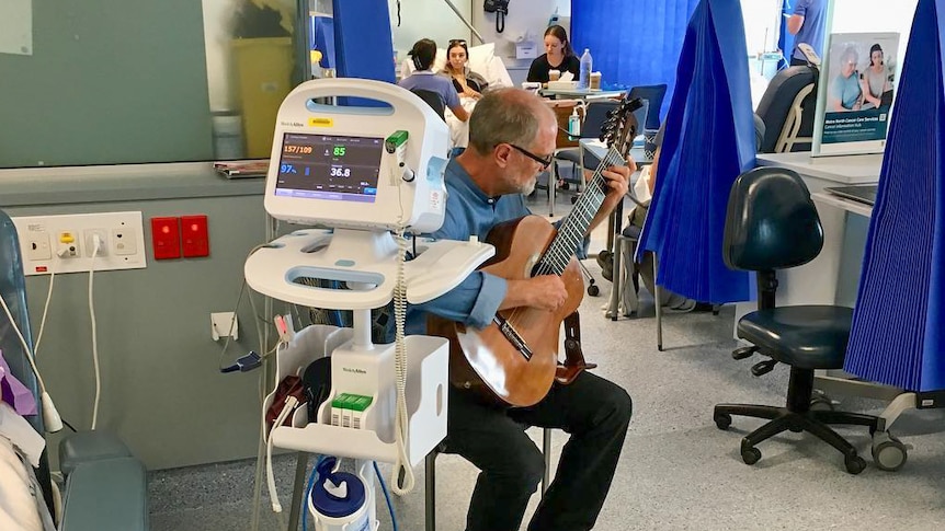 A man playing guitar in a hospital ward.
