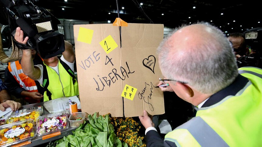 Scott Morrison signs "cheers ScoMo" on a cardboard sign with "vote 4 Liberal"