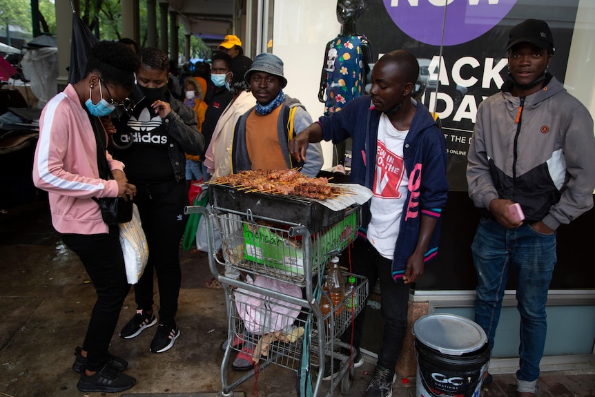 A woman wearing a face mask buys chicken on a crowded sidewalk.