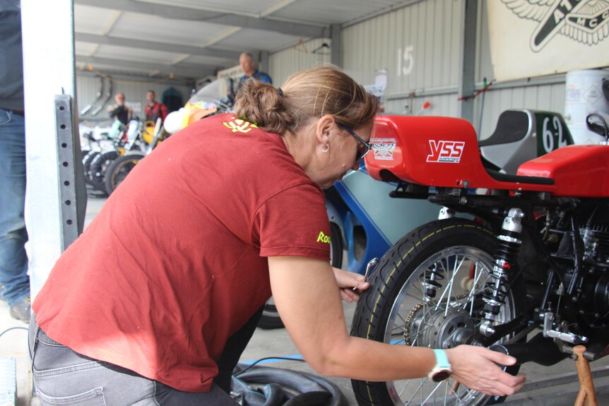 A woman in a maroon shirt kneels next to a motorbike