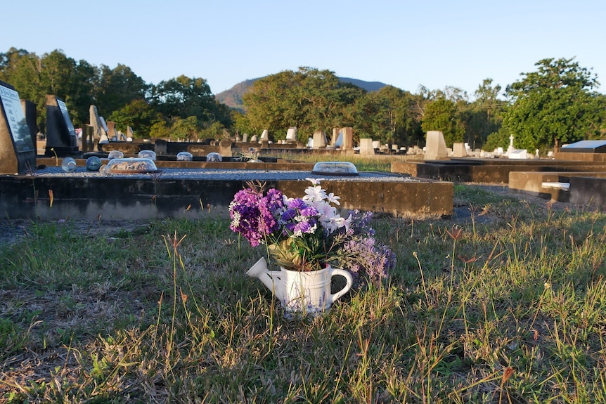 An empty grave plot with a jug of flowers in the middle of the grass