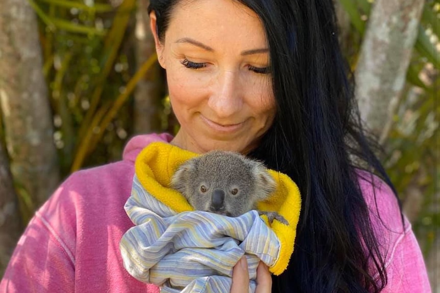 A woman holds a tiny koala joey wrapped in a blanket