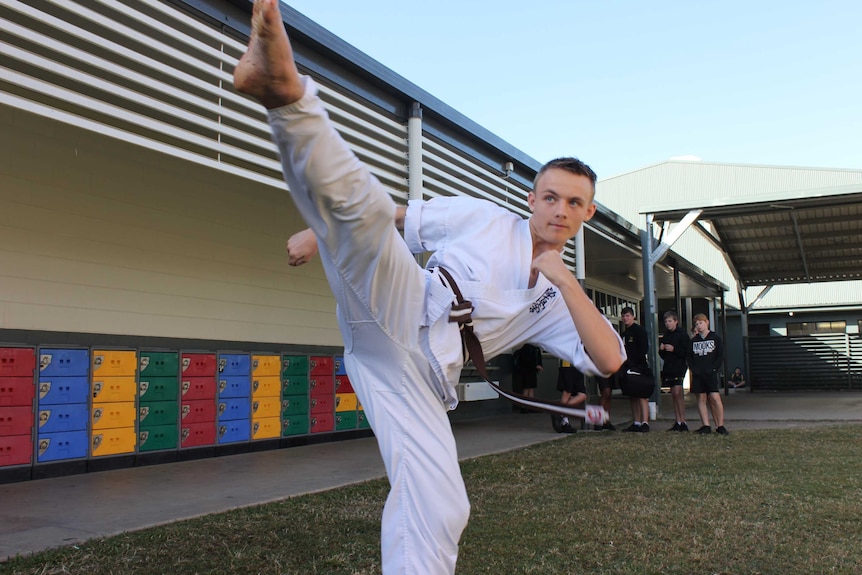 A karate student kicks high in the air while practicing on grass.