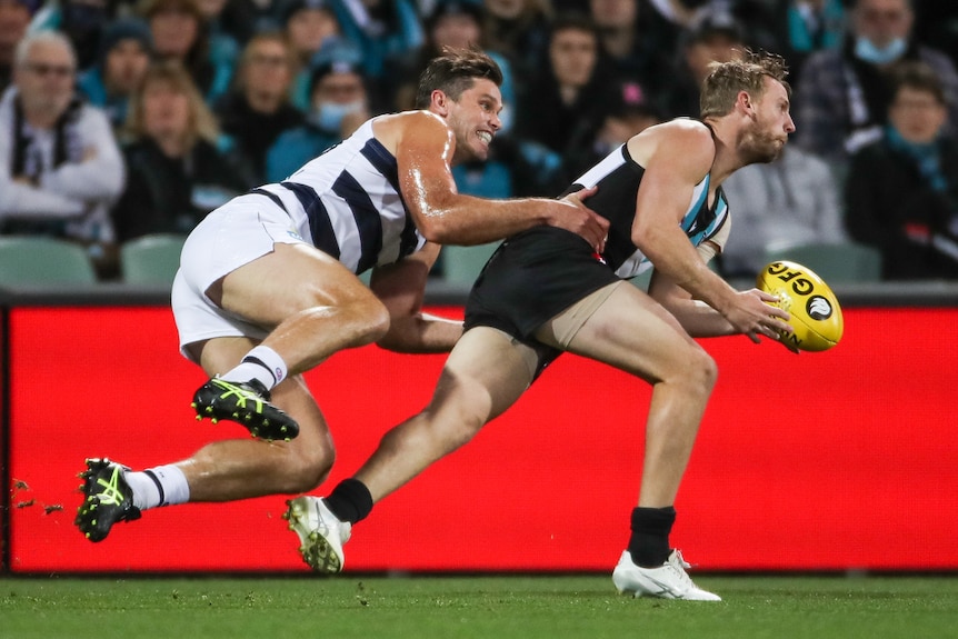 A Port Adelaide holds the ball as he is tackled by a Geelong opponent.