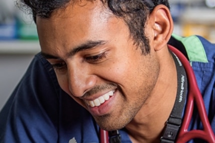 A doctor with a stethoscope around his neck smiling as he looks down.