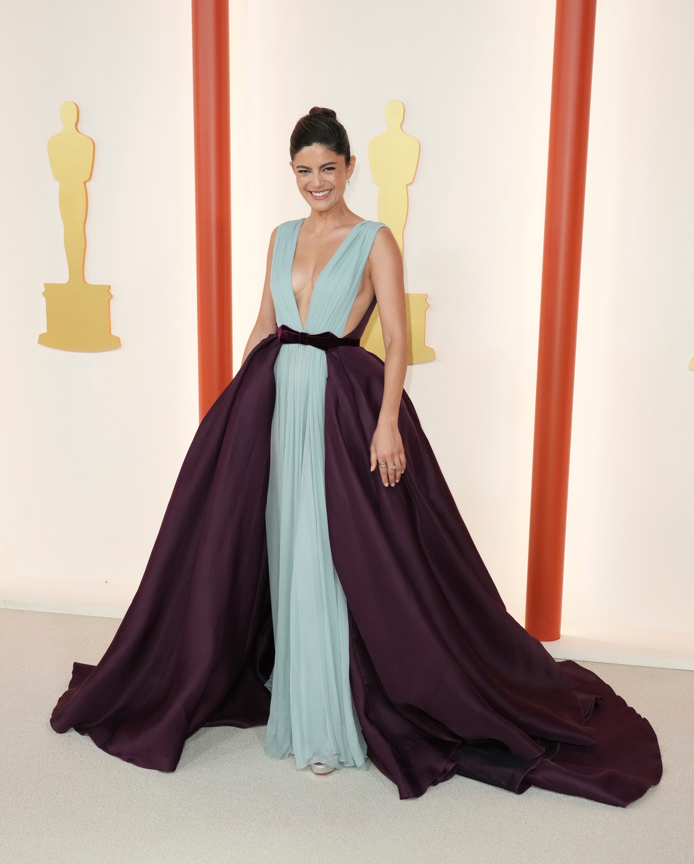 Monica Barbaro wearing a pale blue floor-length dress with a dark purple flowy skirt over the top
