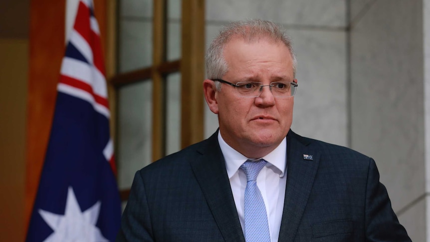 Scott Morrison stands at a lectern in a courtyard with an Australian flag behind him