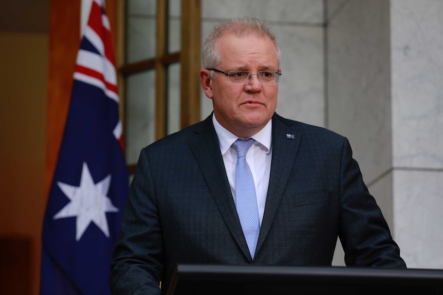 Scott Morrison stands at a lectern in a courtyard with an Australian flag behind him