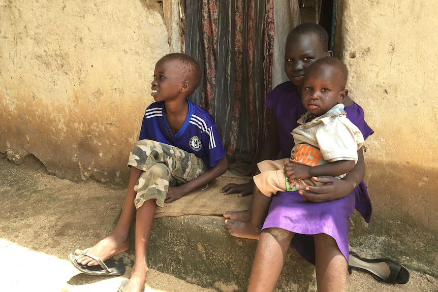 Three young children sit on steps outside a run down building in South Sudan.