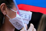 A woman wears a facemask that says "free Navalny" on it, she is holding a Russian flag.