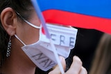 A woman wears a facemask that says "free Navalny" on it, she is holding a Russian flag.