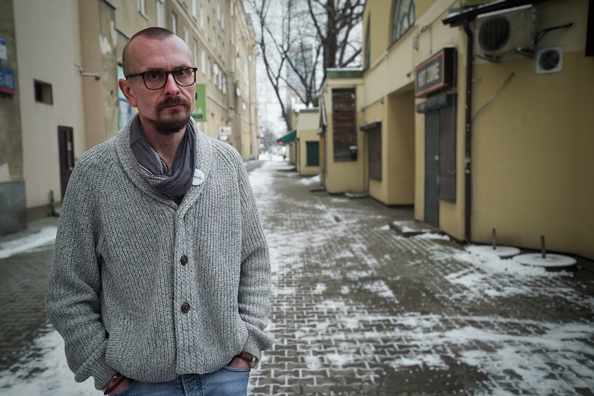  Konrad Korzeniowski stands in a snowy city street in a grey woolly jumper and glasses, with a neutral expression