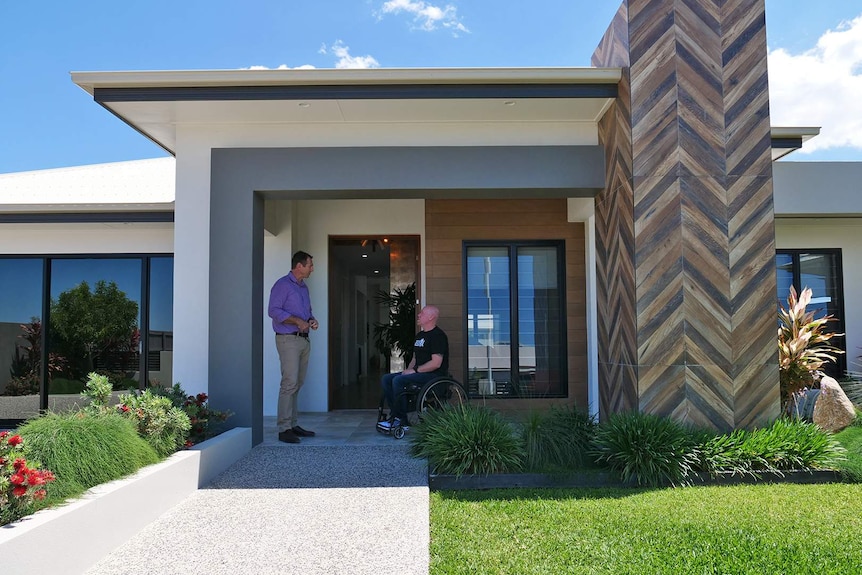 Two men talk in the doorway of a house, one man is in a wheelchair.