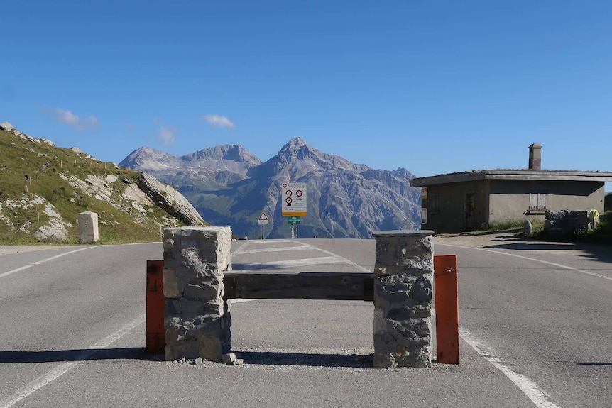 On a bright blue day, you view an empty mountaintop road looking at a dormant border crossing.