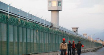 A wide shot shows watch towers and barbed wire fence around a building.