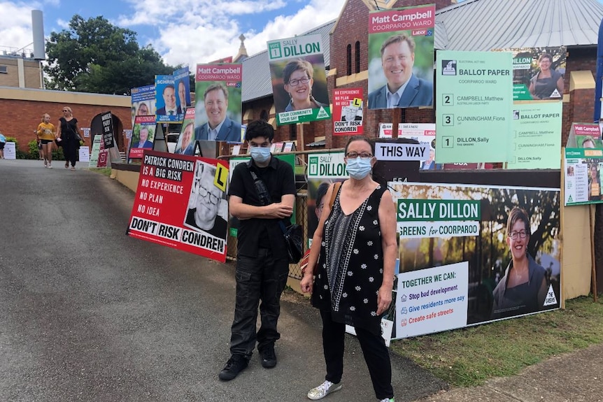 A woman and a man wearing flu masks standing in front of election signs