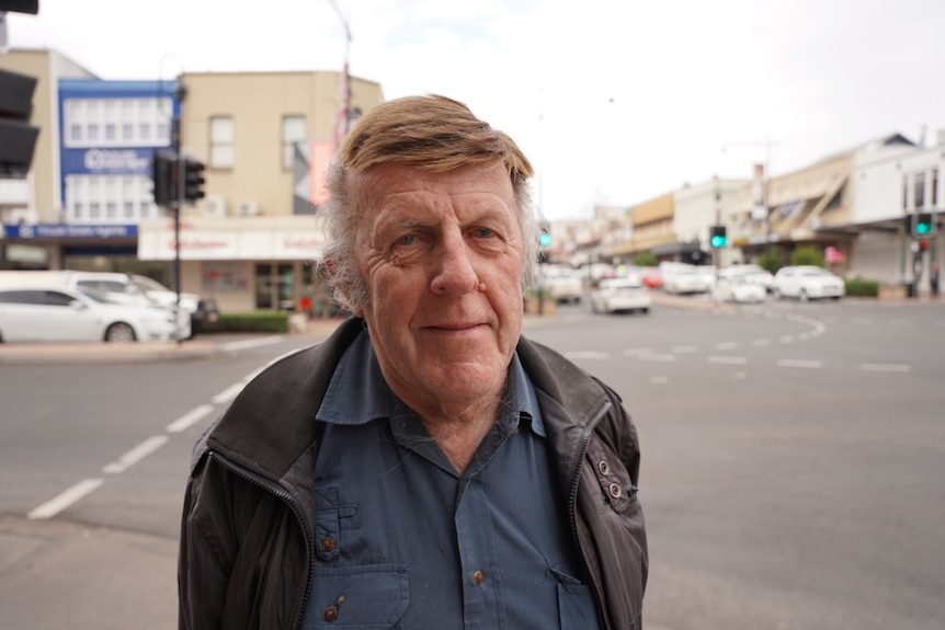 An older man with brown hair standing on a footpath with the street visible behind him