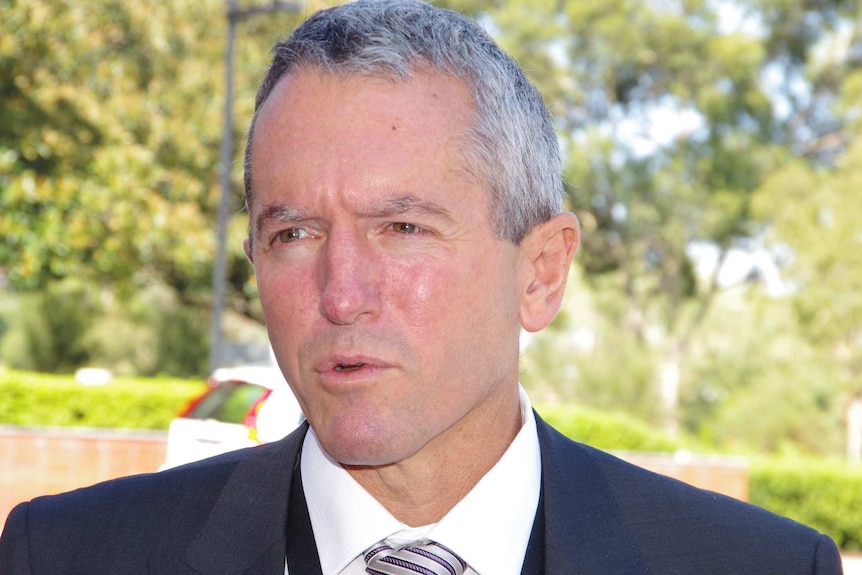 A man in a suit and tie speaks at an outdoor press conference.