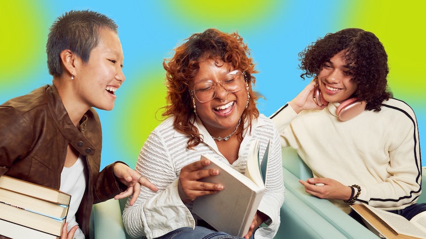 A stock image of a book club, with three people, two women and a young man, looking at a book and laughing