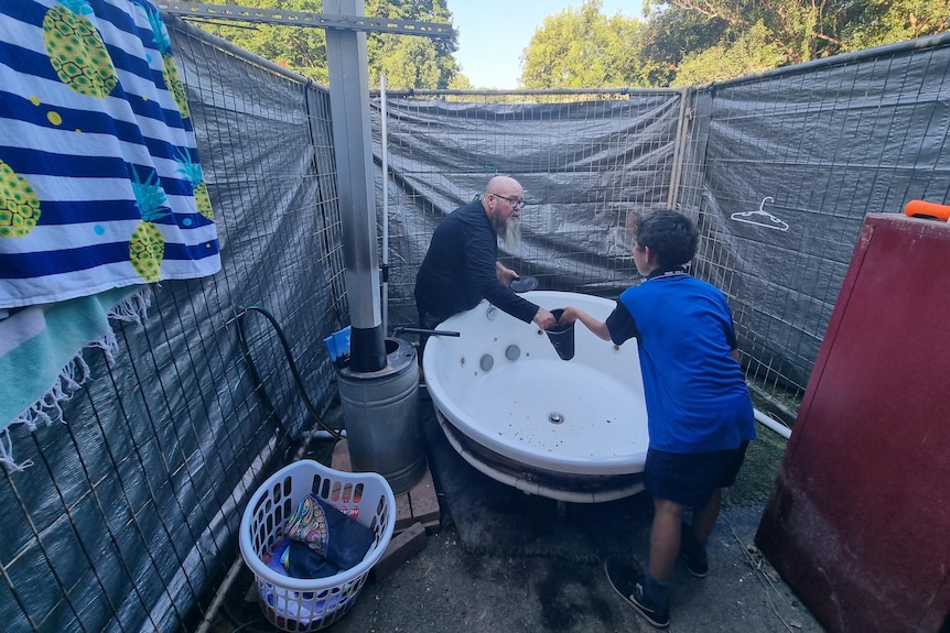 man and child lean over a makeshift bath outside a property