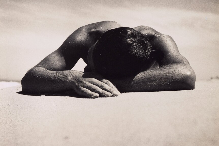 Black-and-white image of a man sunbaking on a beach.