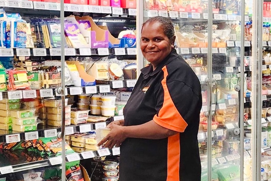 An Indigenous woman stacks shelves at a grocery store smiles at camera