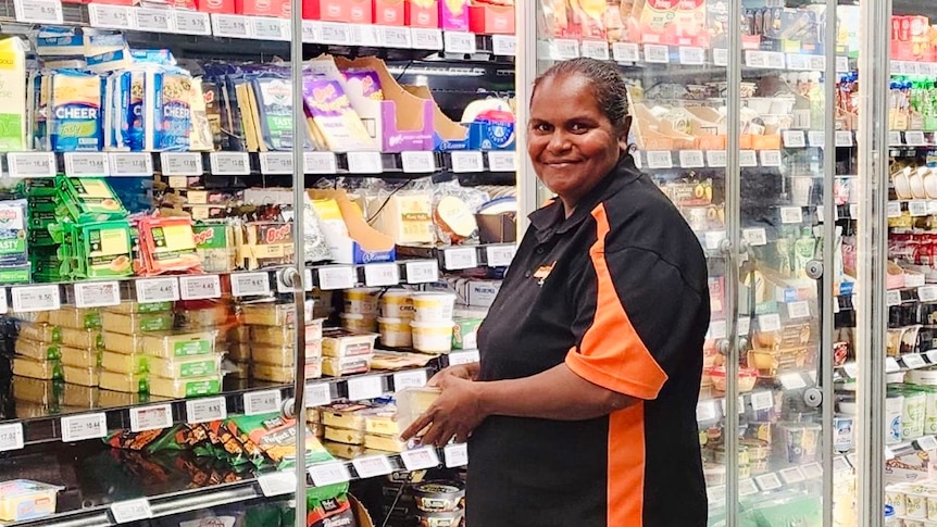 An Indigenous woman stacks shelves at a grocery store smiles at camera