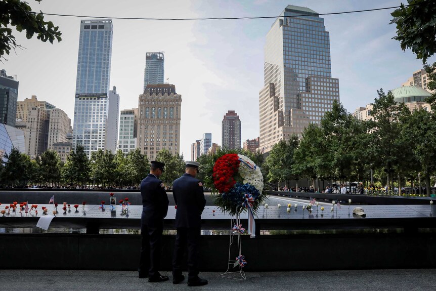 New York City Firemen pause at the edge of a reflecting pool at the National 9/11 memorial.