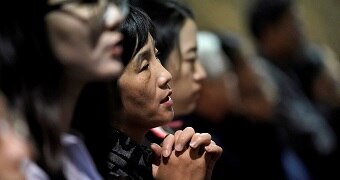 A woman clasps her hands together as she prays.