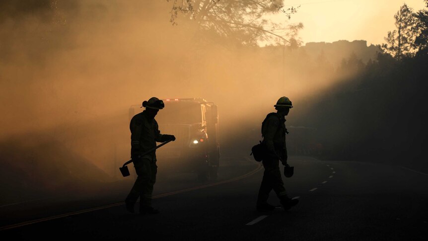 Two firefighters walk along the edge of a road looking for any potential fire breakouts