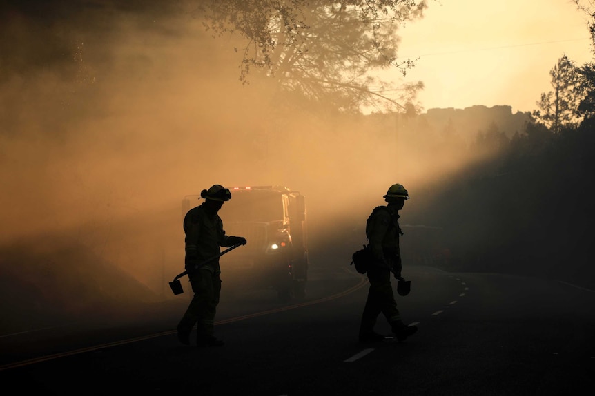 Two firefighters walk along the edge of a road looking for any potential fire breakouts