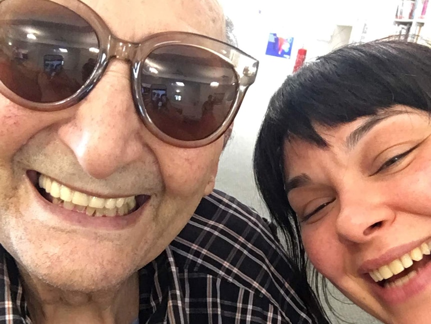 Selfie taken of an older man wearing large sunglasses smiling next to younger woman laughing