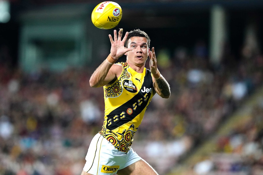 A Richmond Tigers AFL player holds out his two hands as he looks to catch the ball against Essendon.