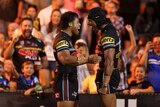 Two NRL players embrace in a hug, in front of a packed grandstand, at night