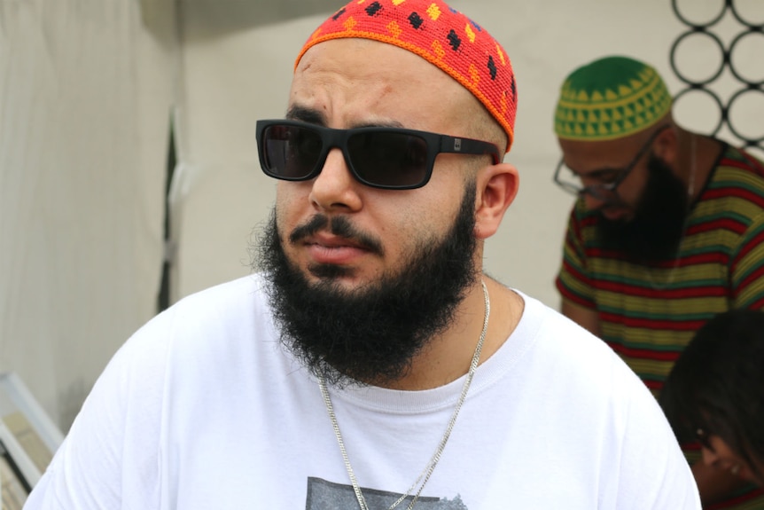 A man with sunglasses and an Islamic cap.