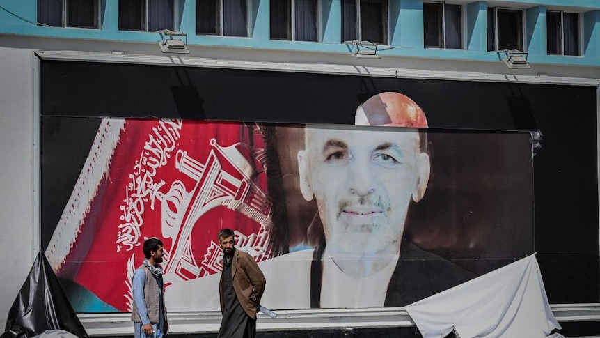 Afghan men stand next to a torn poster of Afghan president Ashraf Ghani at the Kabul airport in Kabul