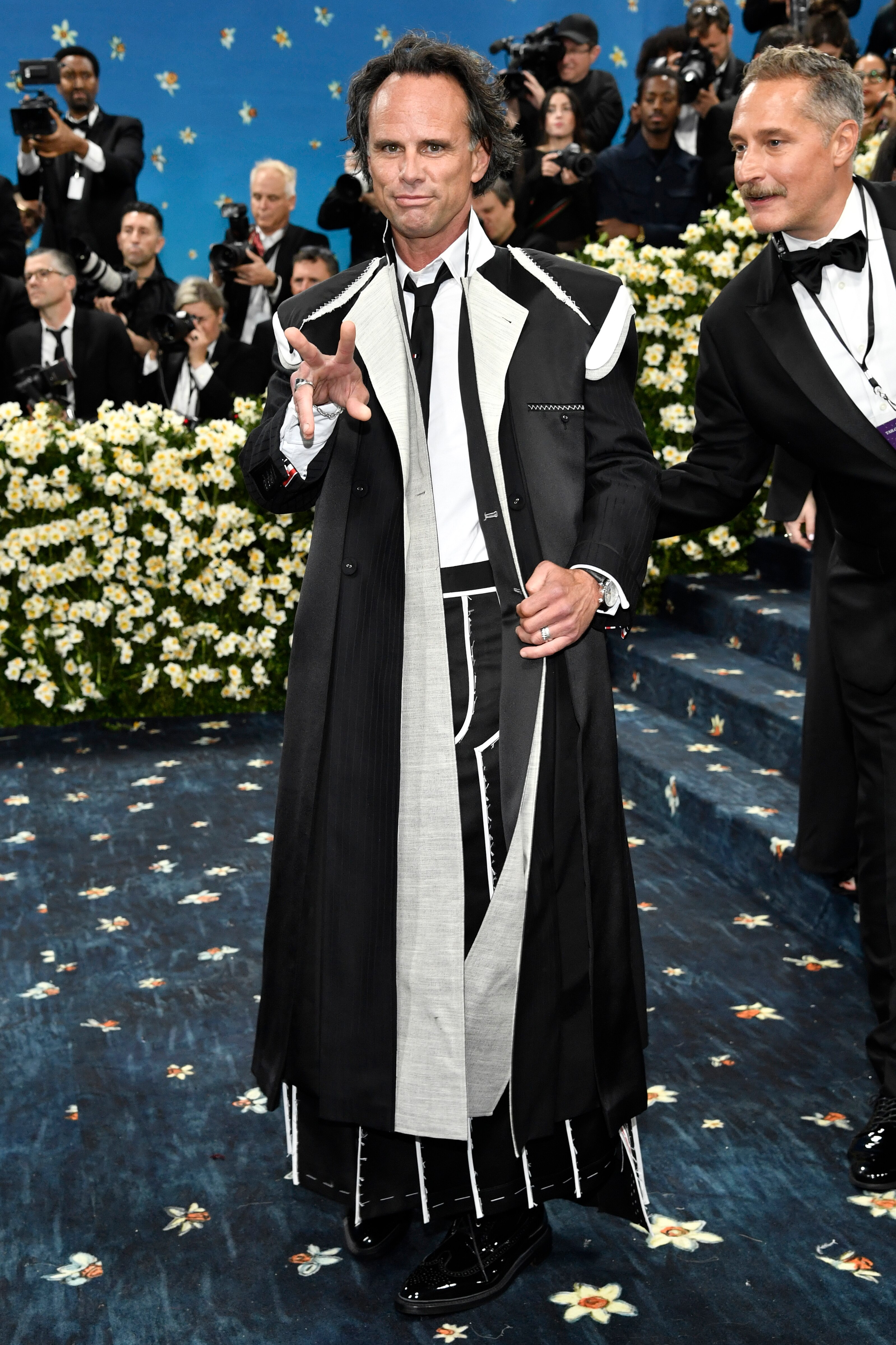 Walton Goggins wearing a long black cape-like suit jacket with a black tie