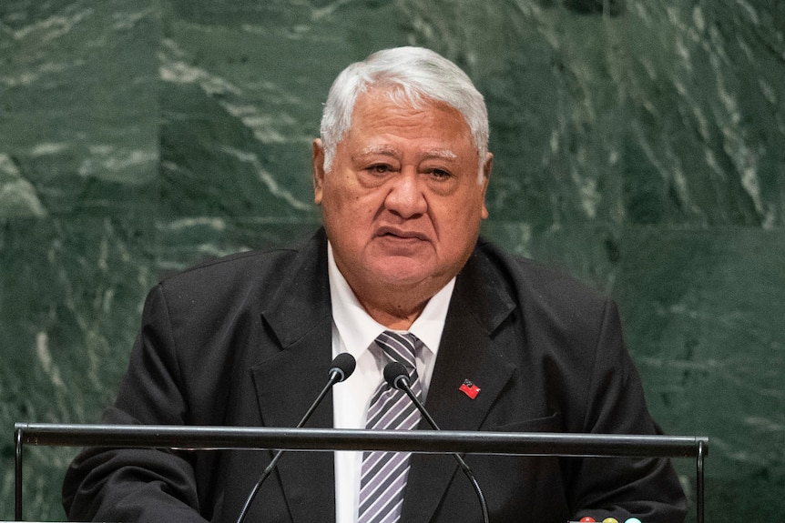 Man in suit stand in front of microphones at podium.